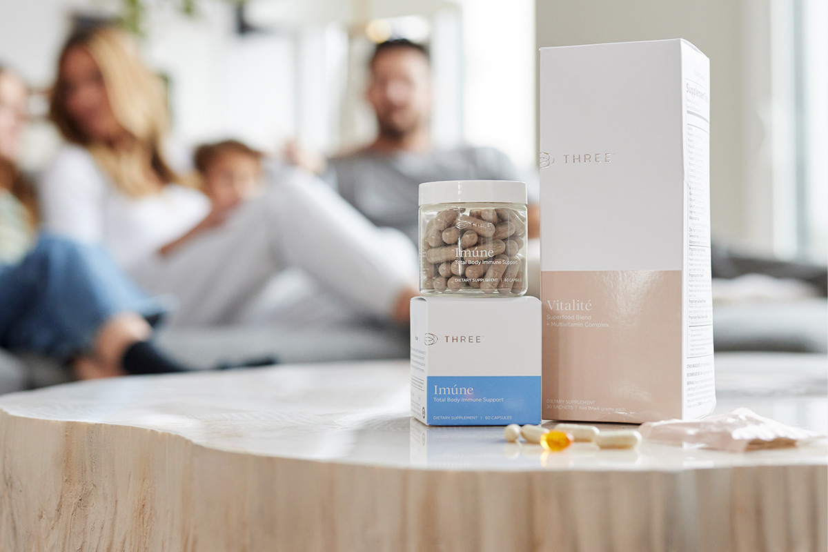 Three supplements sitting on a log table with a happy family in the background